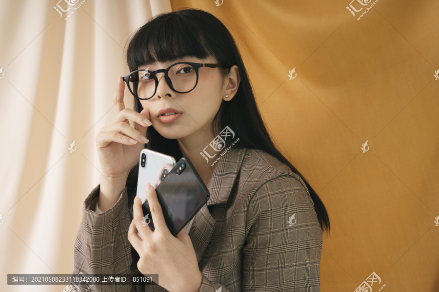 美丽的亚泰黑发女子戴着眼镜手持智能手机。时尚肖像。西装外套。倾斜眼镜。