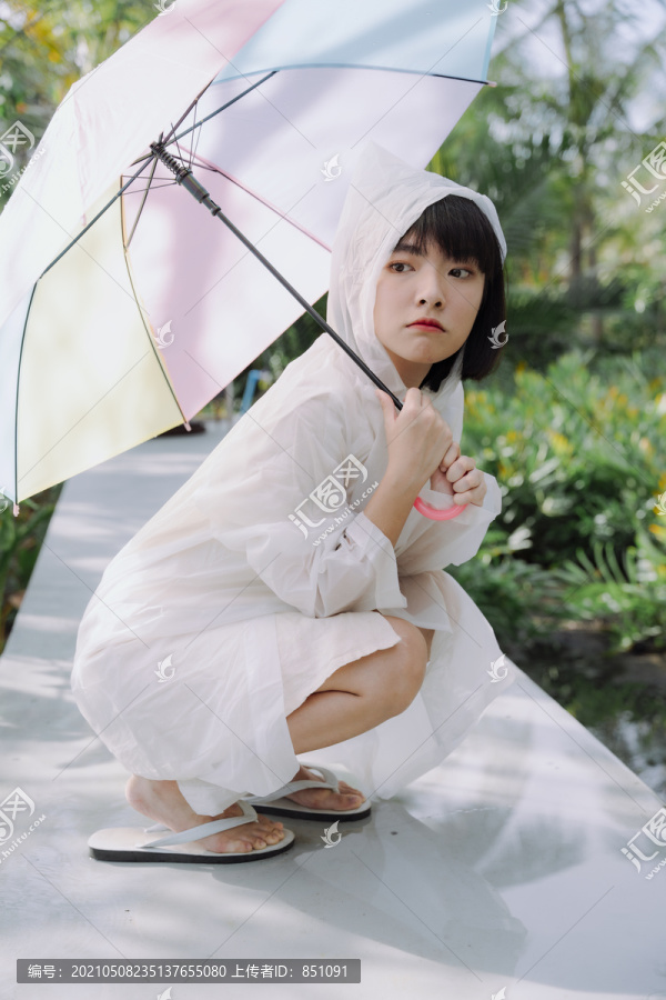 美丽的亚泰女子黑色短发，穿着雨衣，手持雨伞。坐姿。