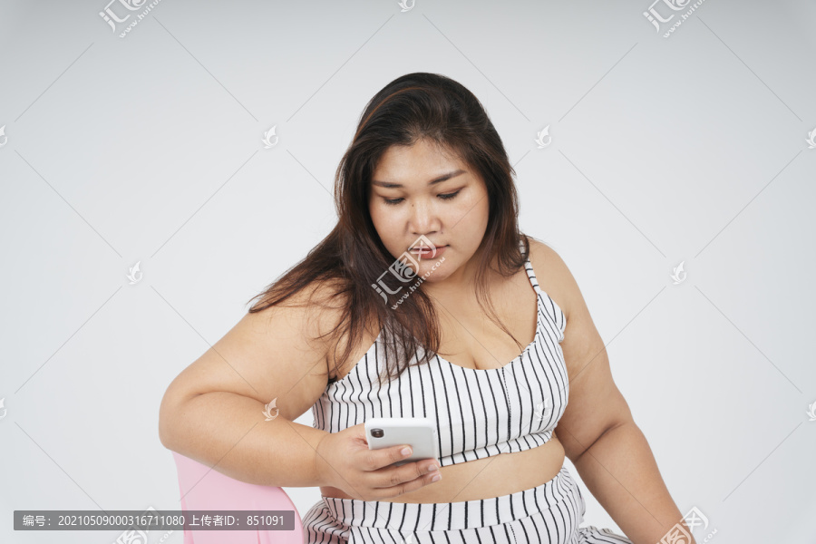 健康的亚洲胖女人坐在椅子上用白色背景的智能手机拍摄的肖像。