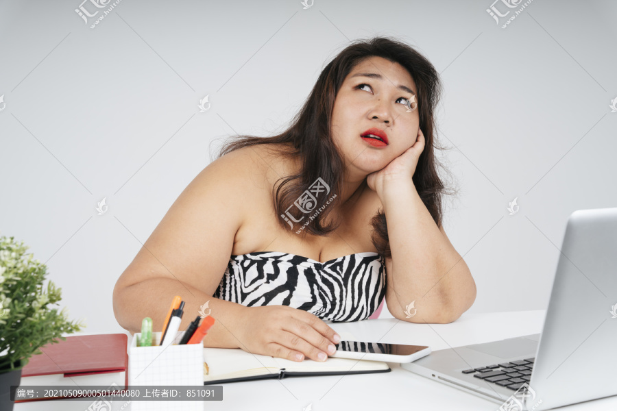 心烦意乱的亚洲胖女人坐在办公室的办公桌旁，抬起头来。