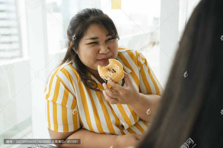 亚洲胖女人喜欢和办公室里的朋友一起吃不健康的甜点甜甜圈。