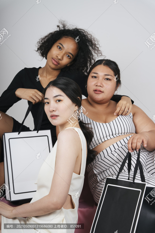 三位不同女性的集体肖像，亚裔和非洲人拿着购物袋做模型。