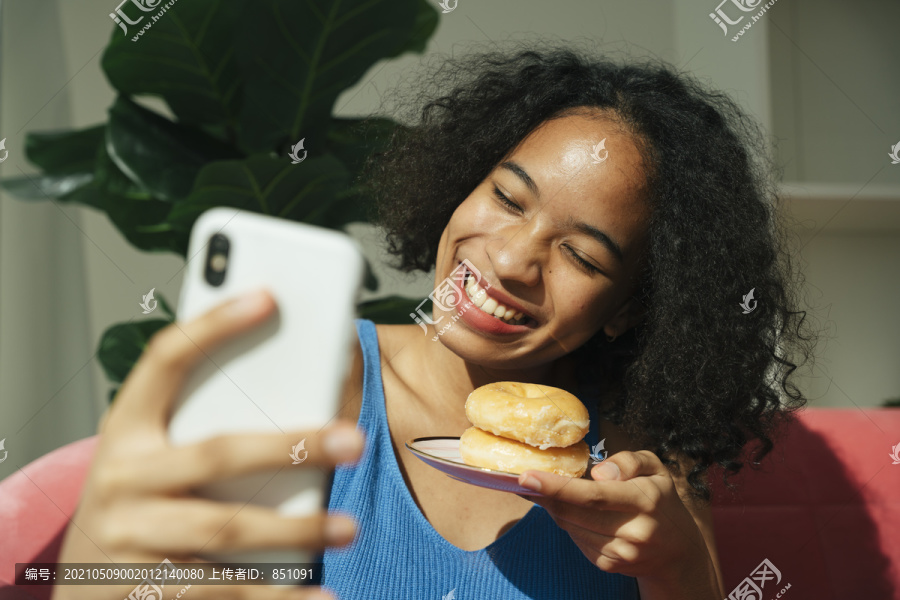 非洲卷发女人在智能手机上直播吃甜甜圈。食物贩子。