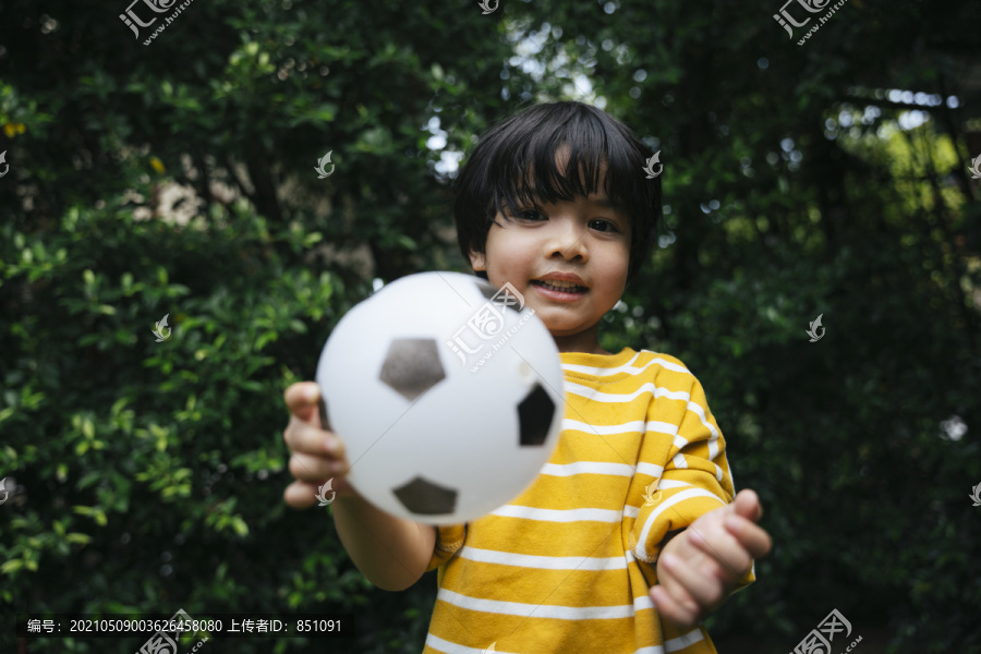 穿着黄衬衫的亚洲男孩在公园里踢足球的肖像。
