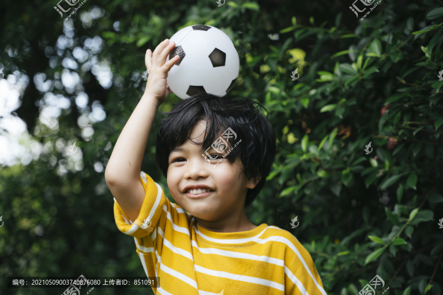 快乐的亚洲男孩举着足球在户外公园微笑。