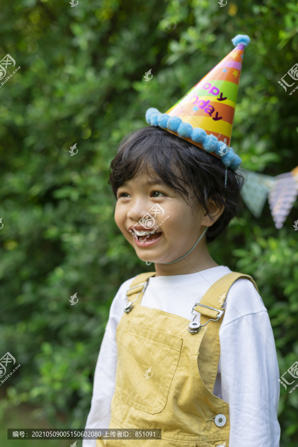 快乐的亚洲人画像黑发小孩戴派对帽微笑着快乐。快乐男孩在户外的院子里庆祝生日。