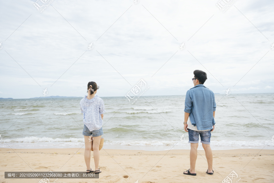 后视图-亚洲夫妇旅行者站在沙滩上看海的水平。