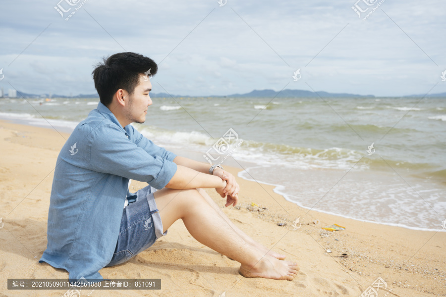 孤独的亚洲人在夏天独自坐在沙滩上看海。