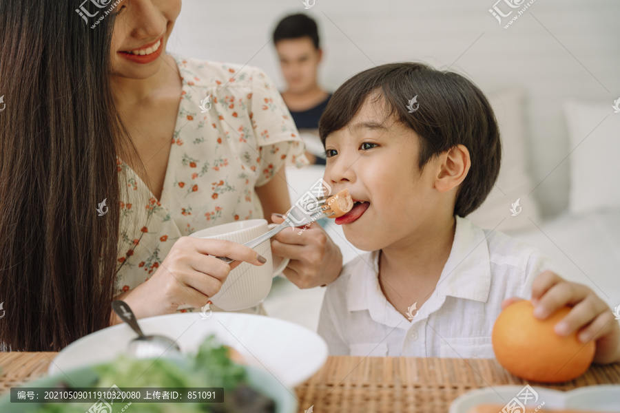 亚泰妈妈给儿子喂饭。一家人在家吃午饭。