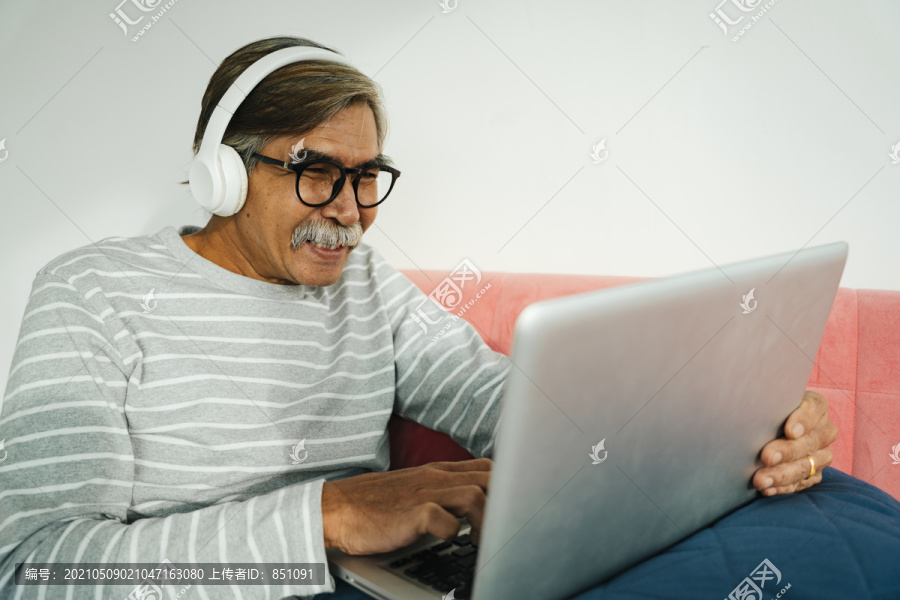 戴着无线耳机的老人在笔记本电脑上挑选歌曲。