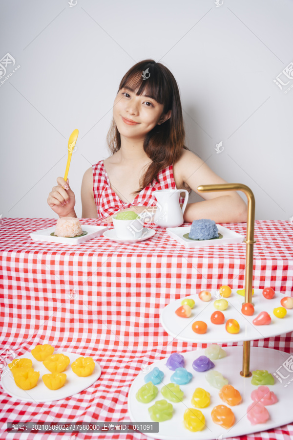 一位年轻的亚洲女士，在粉红色的桌子上摆着许多淡黄色的泰国甜点。