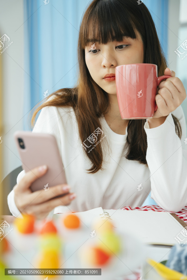 年轻的亚洲黑发女子手持智能手机和咖啡杯。