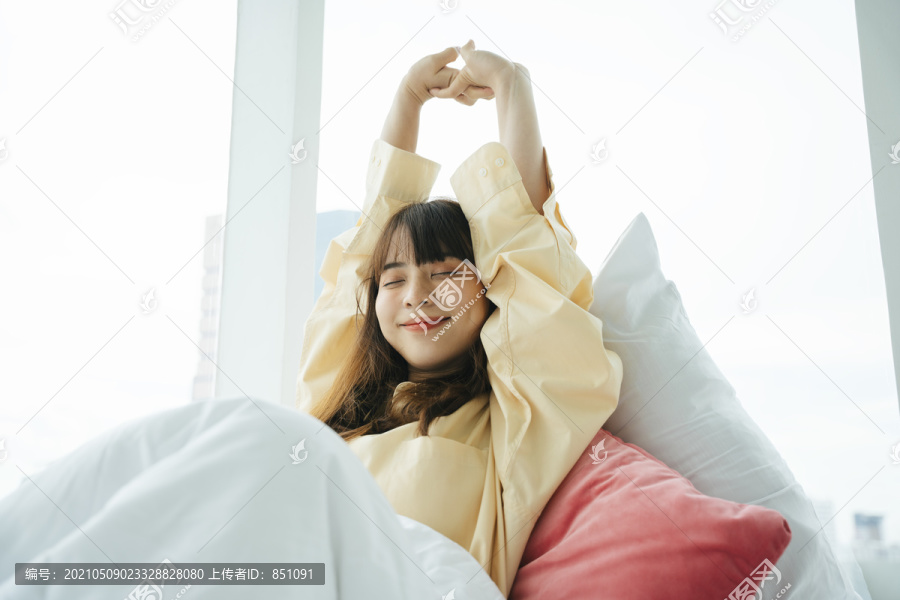 昏昏欲睡的年轻亚洲黑发女子早上起床后伸着手。