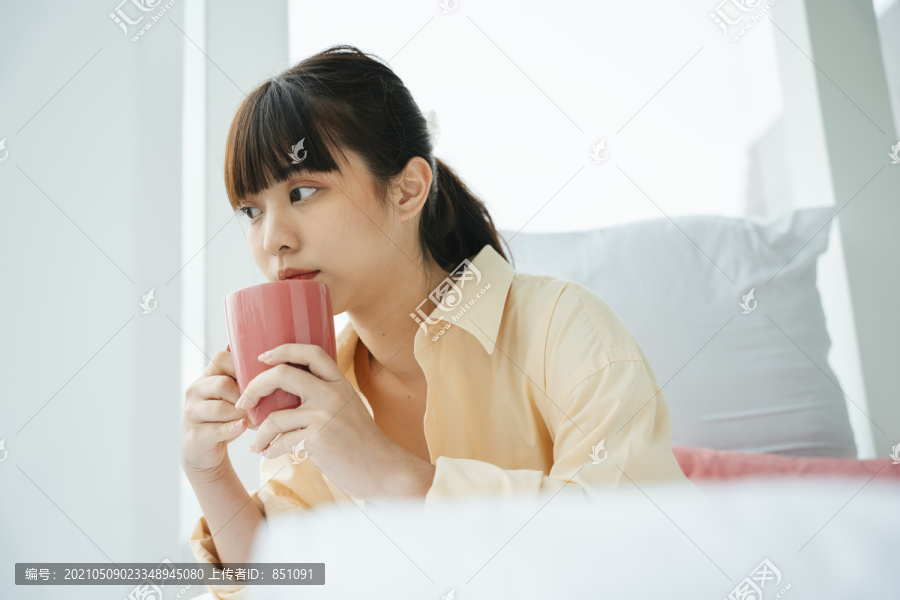 年轻的亚洲黑发女人在卧室里喝咖啡。