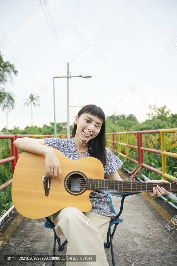 美丽的亚洲年轻女子在户外大自然中弹吉他的画像。