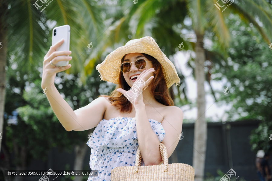 美丽的亚洲女旅行者戴着帽子和太阳镜用智能手机做旅行视频博客。