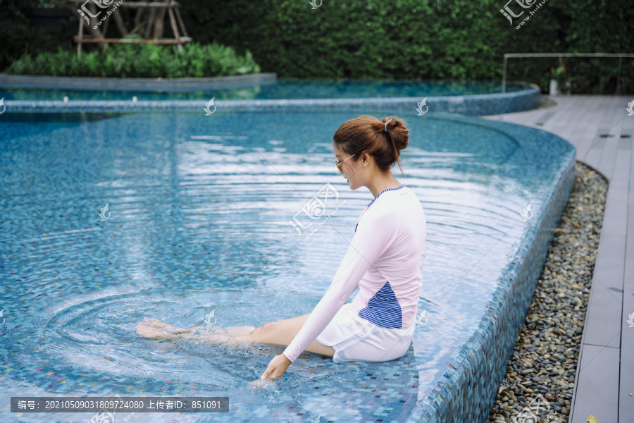 美丽的亚洲女游客穿着游泳衣坐在室外游泳池边。