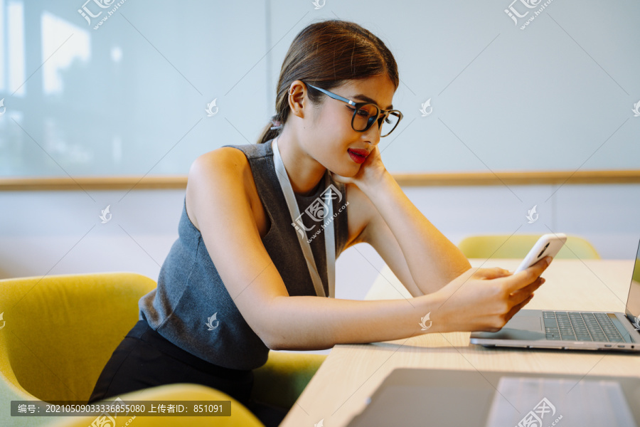 侧视图-亚洲女商人在办公室使用智能手机戴眼镜。