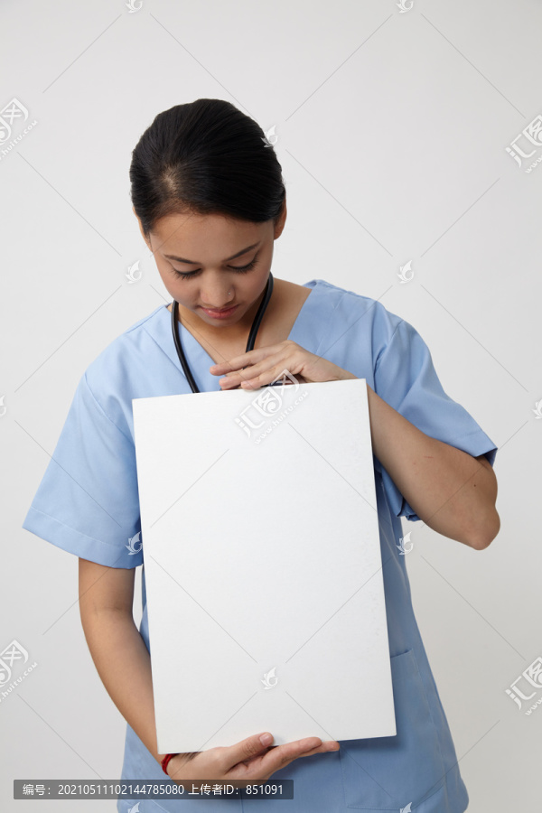护士站着展示医疗标志的广告牌，年轻微笑的女护士或医生在擦洗台上展示空白的带有复印空间的广告牌。白色背