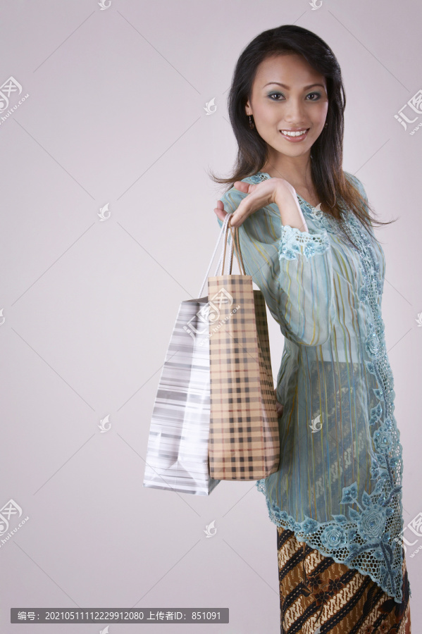 一位年轻的马来妇女手拿购物袋，背景朴素