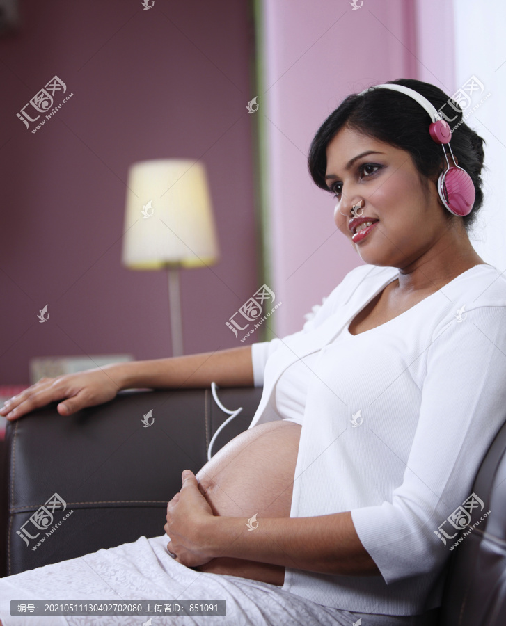 怀孕的年轻女子在家欣赏音乐