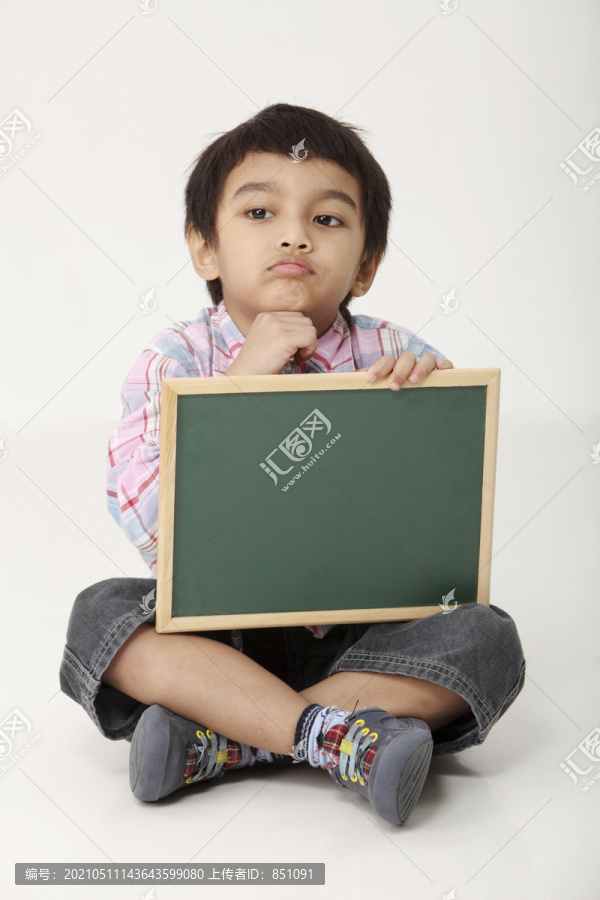 男孩坐着，手里拿着一块黑板，手放在下巴上