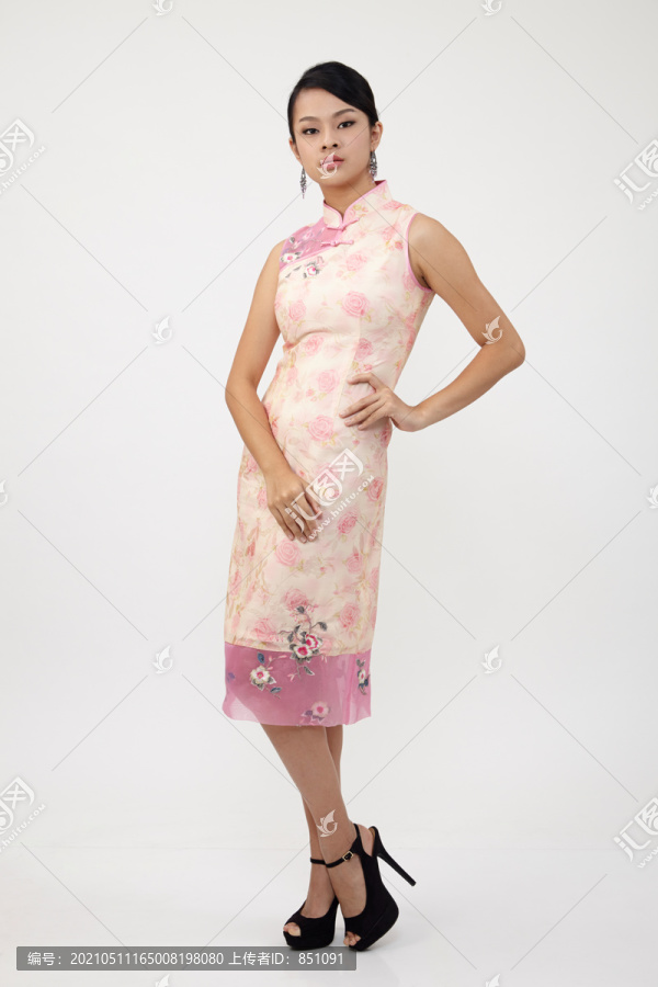 微笑的中国女人穿着传统旗袍摆姿势，摄影棚拍摄的白色背景上的孤立。