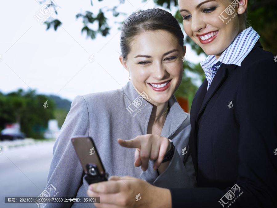 两位商务女士一边用手机一边微笑