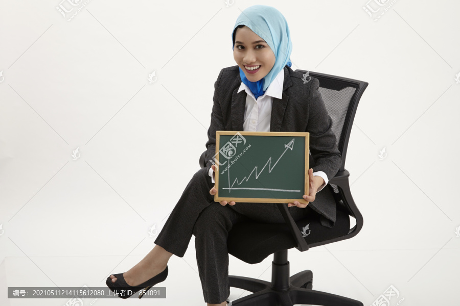 马来女商人坐在办公椅上举着黑板举着图表