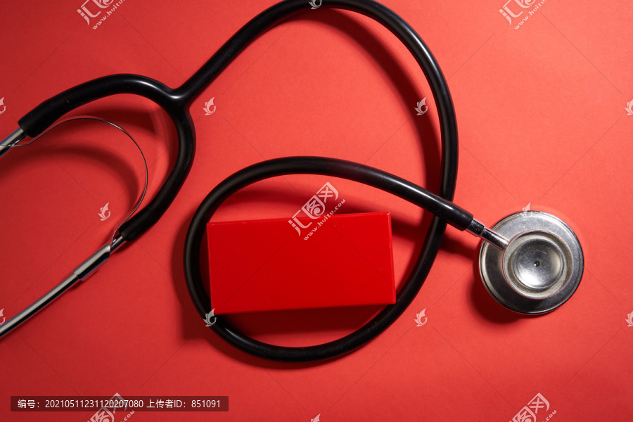 红色背景上的黑色听诊器顶视图，带有复印空间。