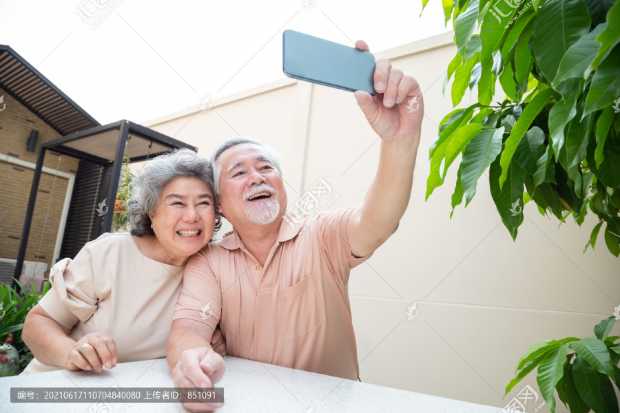 亚洲老年夫妇通过手机视频通话聊天或自拍，老年智能技术和在线行动保持联系的概念