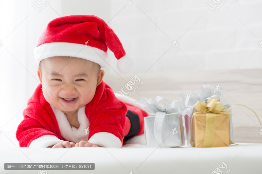 圣诞节和新年快乐时，穿着圣诞老人服装的亚洲男婴躺在白色的床上