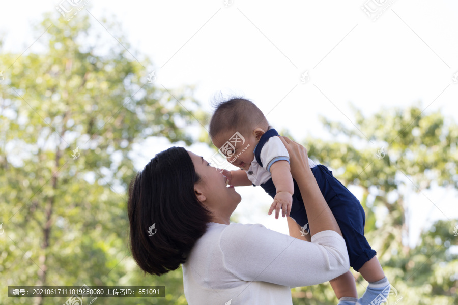 在绿色花园的夏日里，快乐的年轻母亲和小儿子一起玩耍。公园中的家庭概念