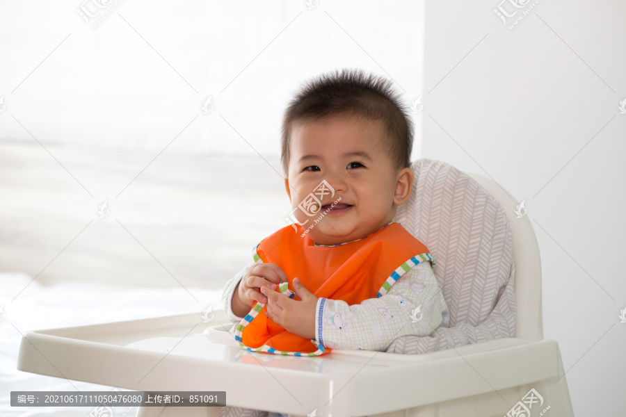 快活快乐的亚洲宝宝等着吃东西，坐在儿童椅上
