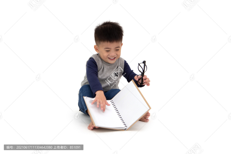 一个可爱的亚洲小男孩坐在地板上读一本白色背景下的书，回到学校的概念，1岁10个月大