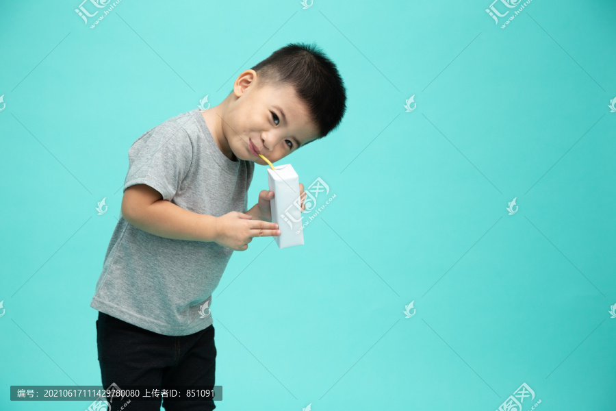 可爱的亚洲小男孩抱着牛奶盒，吸吮着隔离在绿色背景上的牛奶管