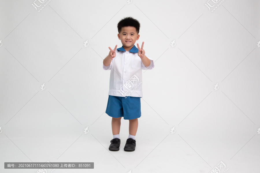 穿着学生制服的亚洲小男孩，在白色背景上显示两个手指孤立的标志，幼儿园第一天和返校概念，泰国男孩模型