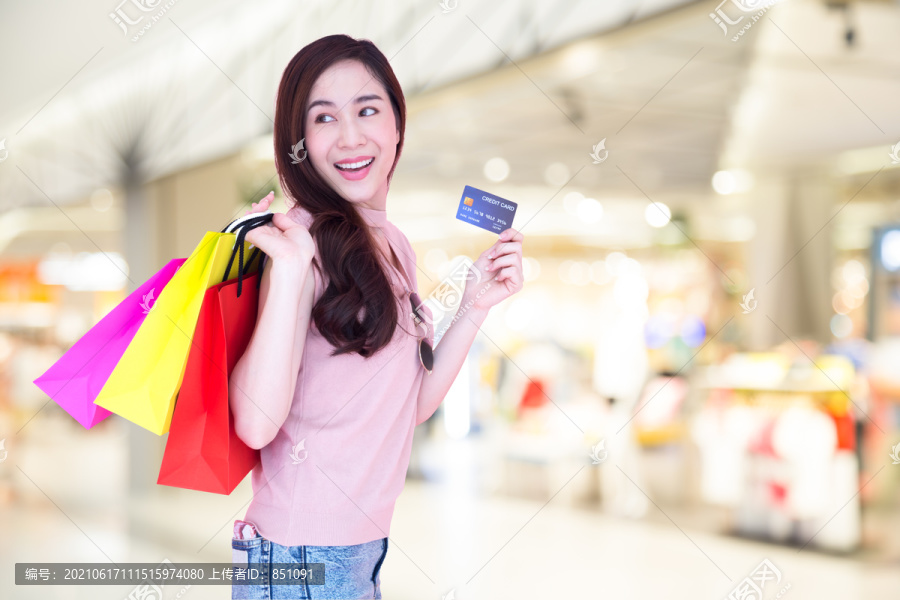 快乐美丽的亚洲女性在购物中心背景下享受购物和持有信用卡，购物狂，年终促销期间购买，年中特价，消费主义