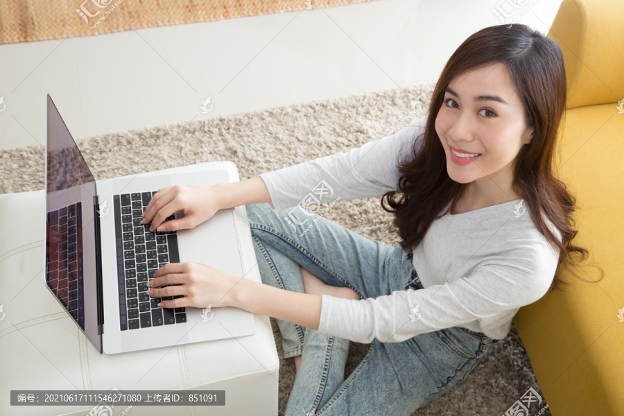 快乐美丽的亚洲女性坐在客厅的地板上使用笔记本电脑，自由职业女性在家使用笔记本电脑，博客或博客在社交媒