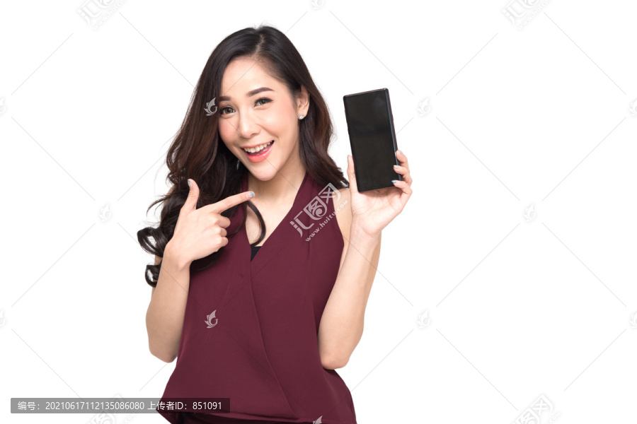 一位穿着红色连衣裙、兴高采烈的美丽女孩的肖像，展示或展示手机应用程序，并将手指指向手上的智能手机，与