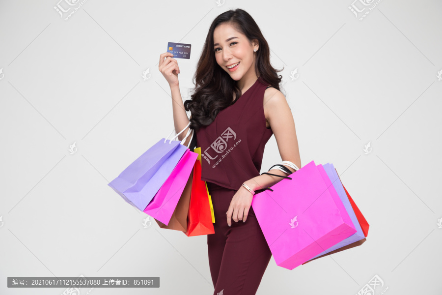 一位身穿红色连衣裙、手持购物袋和信用卡的快乐年轻亚洲女性的肖像，与白色背景隔离，年终促销或年中促销活