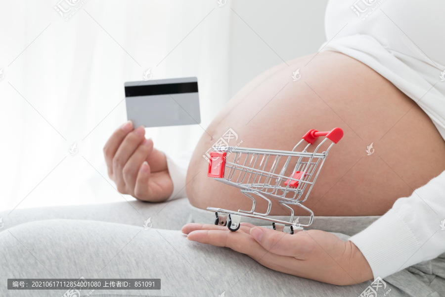 孕妇在出生前准备购买婴儿用品，将购物车和信用卡放在肚子前，在怀孕期间和产前准备购物清单