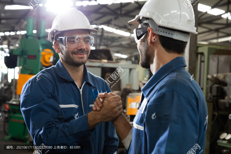 戴手套的重工业工人在金属制品工厂相互握手问候，团队合作和伙伴关系理念