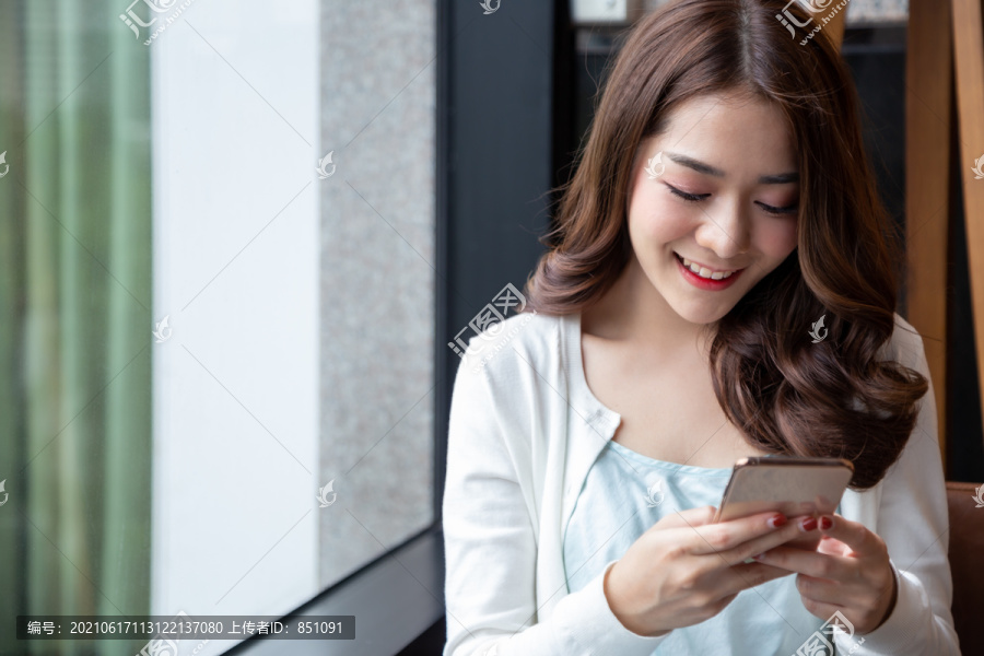 在咖啡馆休息时，迷人的亚洲女人微笑着在手机上读着好消息