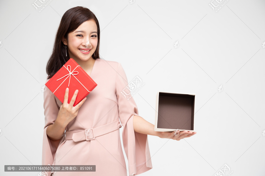 快乐美丽的亚洲女人微笑着，拿着白色背景上的礼品盒。少女坠入爱河，接受情人的礼物。新年、圣诞节和情人节