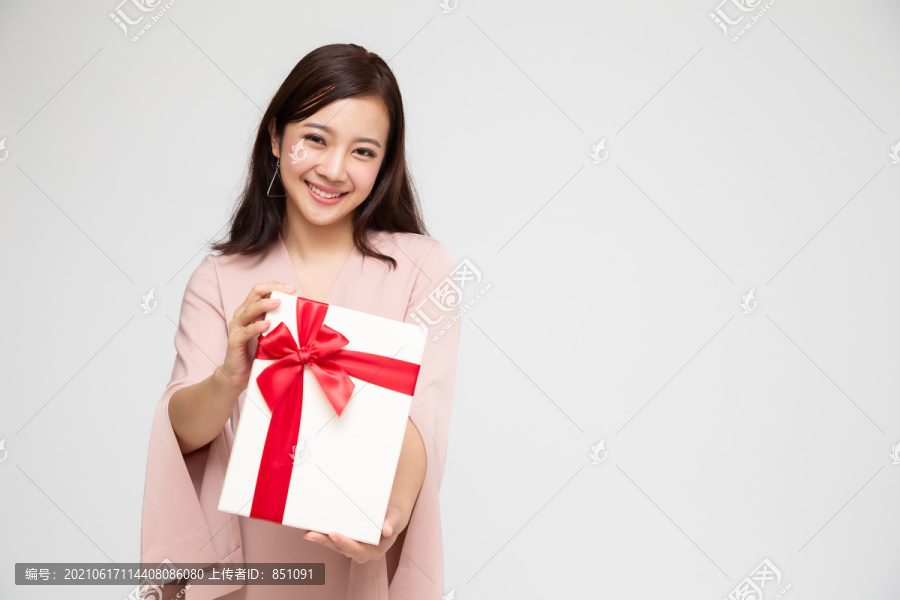 快乐美丽的亚洲女人微笑着，白色背景上有一个孤立的礼品盒。少女坠入爱河，接受情人的礼物。新年、圣诞节和