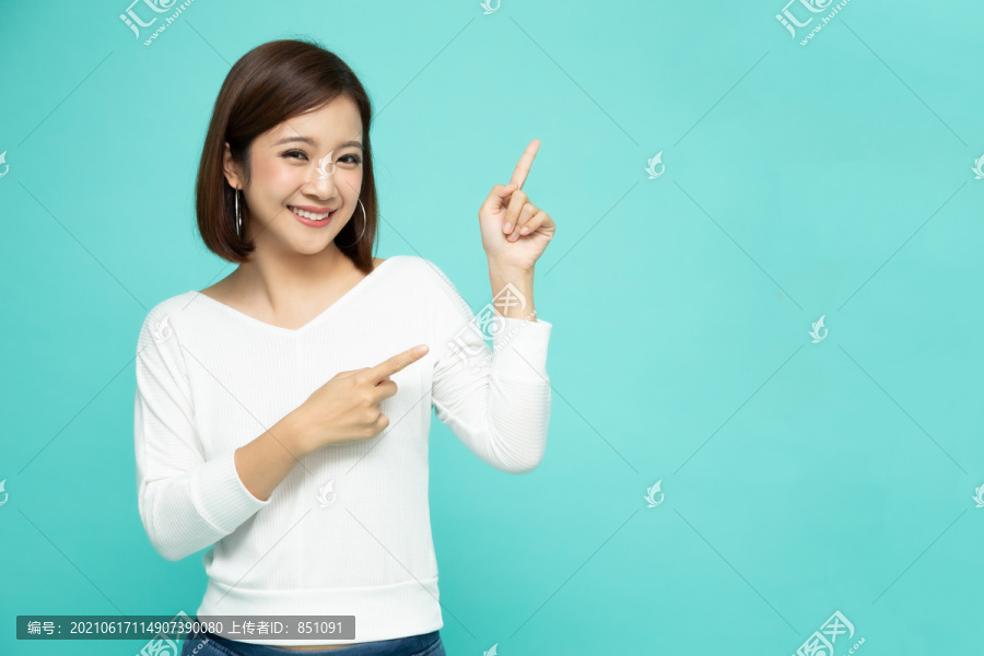 年轻优雅的亚洲女性微笑着指着绿色背景上孤立的空白拷贝空间