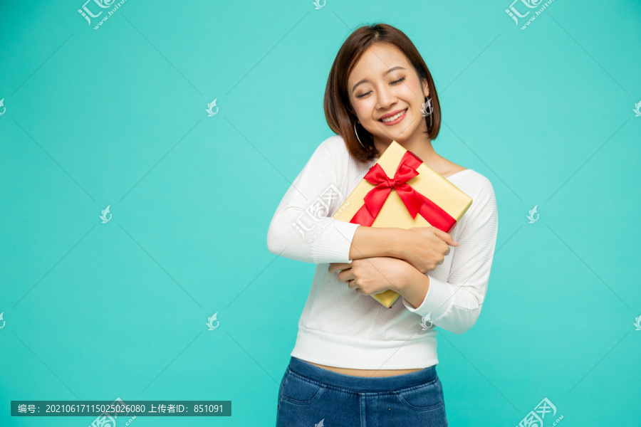 快乐美丽的亚洲女人微笑着，绿色背景上有一个金色的礼品盒。少女坠入爱河，接受情人的礼物。新年还是圣诞节