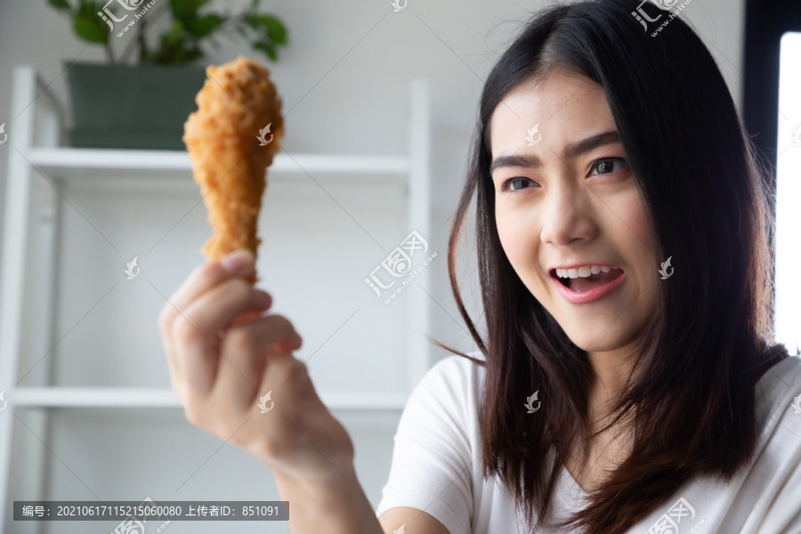 年轻的亚洲女人在家里的房间里吃鸡肉，感受着幸福和喜悦
