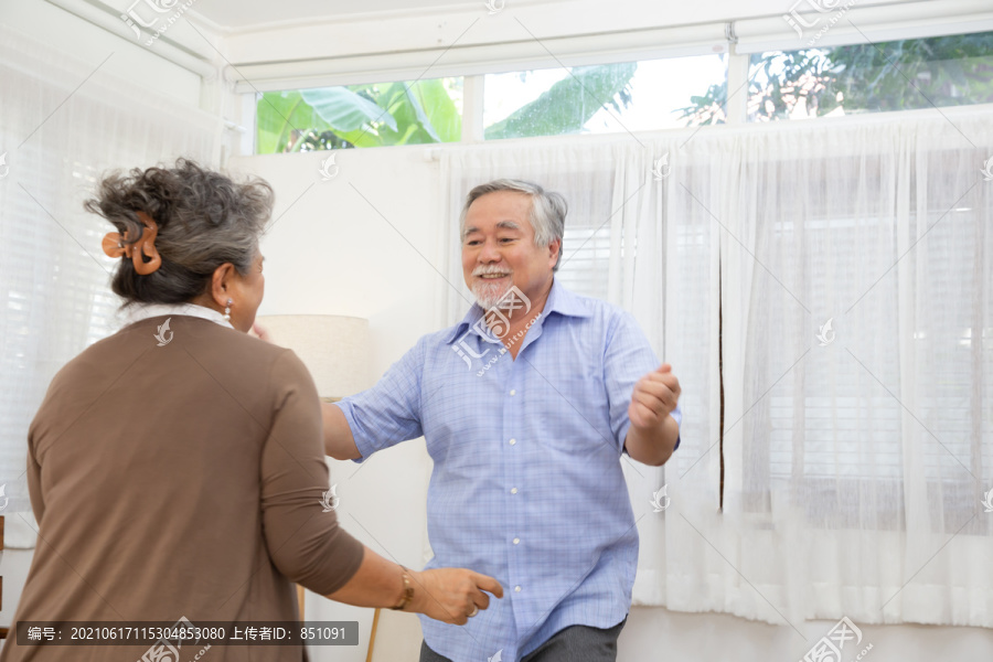 亚洲老年夫妇在家里的客厅里跳舞，快乐成熟的老年人享受着舞蹈的理念
